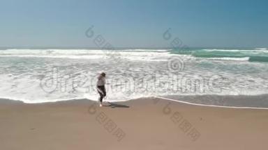 在靠近林肯市的俄勒冈州海岸的巨浪中，海滩上一位年轻的时髦女子奔跑的空中镜头。
